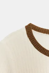 Top de tejido rústico con cuello redondo y manga corta. Presenta un diseño de base color crema con detalles de rayas horizontales en tonos marrón y lila en el pecho y los puños.