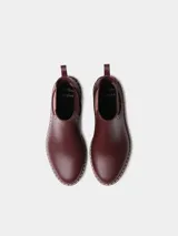 Botas de agua de caña baja color bordó, con elásticos laterales a rayas en tonos burdeos, beige y marrón. Cuenta con suela dentada negra, costuras blancas decorativas en el borde y presilla trasera para facilitar el calce.