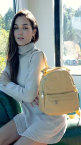 Mochila de tamaño mediano en color amarillo, confeccionada en símil cuero. Presenta un compartimento principal con cierre metálico, un bolsillo frontal con cierre y broche, y bolsillos laterales. Incluye correas regulables para la espalda, asa de mano y una correa adicional para llevar al hombro.