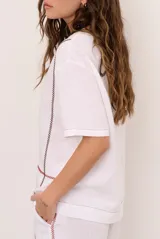 Blusa de lino color beige, de corte recto y mangas cortas, con costuras decorativas pespunteadas en tono rojizo que forman líneas verticales y horizontales.