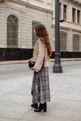 Falda midi de diseño asimétrico que combina paño gris liso con un panel lateral de tela escocesa en tonos grises, marrones y blancos. Presenta un corte irregular con bordes desflecados y tajos laterales.
