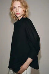 Camisa de cuello redondo y manga corta abullonada, color negro, de corte recto con aberturas laterales y cierre frontal con botones. Perteneciente a la colección ZARA Woman Collection.