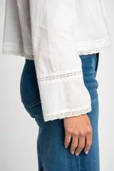 Blusa blanca de algodón con escote en U y mangas largas acampanadas. Presenta detalles de encaje en el escote, el frente y los puños.