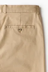 Pantalón de algodón color beige, estilo chino, con corte slim fit. Presenta cierre y botón frontal, bolsillos laterales al bies y bolsillos insertados con botón en la parte trasera.