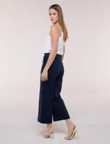 Pantalón crop blanco de corte recto con cintura ancha y botones decorativos laterales. Cuenta con bolsillos y pinzas frontales.