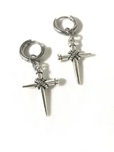 Par de aros colgantes plateados con dije de cruz formada por clavos. El aro es de acero quirúrgico y el dije de aleación.