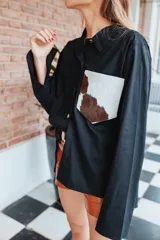 Camisa color naranja de lino o algodón con cuello clásico, cierre frontal con botones y mangas largas con puños abotonados. Presenta un bolsillo de cuero marrón en el pecho.