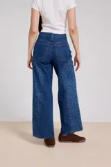 Pantalon de jean azul de corte ancho, con paneles laterales estampados con diseño floral sutil y costuras visibles.