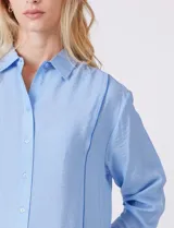 Camisa de algodón con estampado de rayas verticales finas en color azul claro. Tiene cuello con solapa, escote en V y cierre frontal con botones.