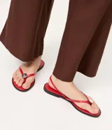 Sandalias planas rojas con diseño de dedo, tiras finas y aplique metalizado decorativo.