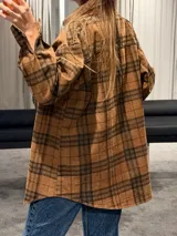 Camisa tipo sobrecamisa de corte oversize, confeccionada en tela a cuadros en tonos marrones y negros. Presenta cierre frontal con botones metálicos a presión, bolsillos frontales con solapa y mangas largas con puños abotonados.