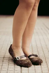 Bailarinas marrones con exterior de pelo sintético y tira de cuero con hebilla metálica.