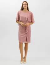 Vestido corto de corte recto con acabado metalizado, confeccionado en tejido ligero. Presenta una sobrecapa de tul liviano sobre los hombros, detalle de pedrería en la cintura, volado lateral y tajo frontal en la falda. Incluye cierre invisible en la espalda y forro a tono.