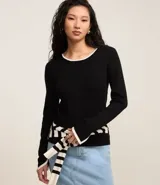 Suéter de punto negro con cuello redondo y mangas largas, caracterizado por detalles de viés en color blanco en el cuello, los puños y el ruedo.