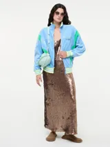 Vestido largo de corte recto con escote redondo y tirantes anchos, completamente cubierto de lentejuelas brillantes. Presenta tajos laterales en el ruedo.