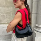 Cartera de hombro negra, estilo baguette, con acabado charol y textura de cocodrilo. Posee correa corta ajustable con detalle de nudo y herrajes dorados.