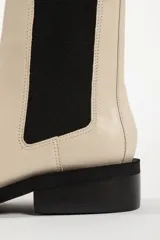 Bota tipo Chelsea de cuero color beige, con paneles laterales elásticos en color negro, puntera cuadrada y suela de goma negra con tacón bajo.