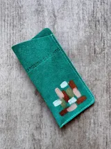 Portalentes de cuero color turquesa, con diseño pintado a mano en tonos cobre, dorado, nude y blanco, y logo de la marca grabado en relieve.
