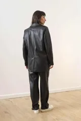 Blazer de cuero sintético color beige, con diseño de doble botonadura, solapas clásicas y bolsillos frontales con solapa.