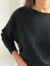 Sweater negro de punto con diseño de mangas tipo murciélago, cuello redondo y puños ajustados. Presenta un sutil patrón de líneas verticales en el tejido.
