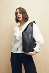 Bolso tipo tote negro de cuero sintético con micro tachas metálicas plateadas. Tiene asas integradas para llevar al hombro.