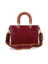 Cartera de mano de estructura rígida con textura símil cocodrilo en color bordó, con manijas superiores cortas en tono tostado y herrajes metálicos dorados.