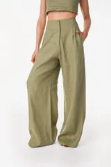Pantalón de lino blanco de corte ancho y fluido, con cintura alta que incorpora una sobrepretina ancha desmontable con pliegues horizontales.