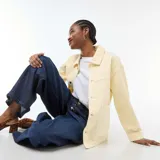 Chaqueta vaquera color amarillo claro, de corte recto y largo medio, con cuello camisero, cierre frontal de botones y dos bolsillos delanteros de parche.