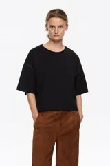 Camiseta negra de corte recto con escote redondo y mangas cortas anchas. Presenta pespuntes a contraste de color marrón claro en las sisas y los bordes de las mangas.