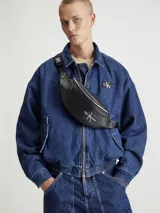 Riñonera negra de cuero sintético con cierre plateado y logo de Calvin Klein Jeans estampado en el frente.