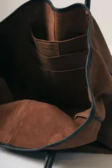 Bolso tipo tote de gamuza color marrón con detalles de bordes y asas en cuero negro.