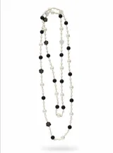 Collar largo estilo Chanel compuesto por una cadena dorada intercalada con perlas blancas, esferas negras y pequeños dijes de flores esmaltadas en blanco y negro.