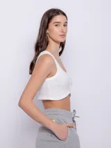 Top blanco de tela texturada, sin mangas y con cuello redondo. Cuenta con cuatro botones y terminación en curva en la parte delantera.