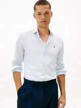 Camisa de Tommy Hilfiger confeccionada en popelín de puro algodón regenerativo con diseño de rayas bengal en tonos celeste y blanco. Cuenta con cuello camisero, cierre frontal de botones y el logo de la marca bordado en el pecho.