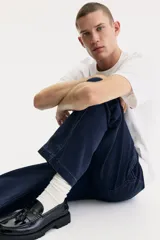 Pantalón tipo worker confeccionado en sarga de algodón de color azul marino, con un corte relaxed fit y piernas rectas. Presenta una cintura clásica con cierre de botón, bolsillos laterales al bies, bolsillos traseros, una trabilla funcional en un lateral y un bolsillo cargo dividido en el otro.