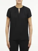 Blusa negra de poliéster reciclado con mangas cortas, cuello redondo, cierre con cremallera en la espalda y abertura en la parte delantera con barra metálica.