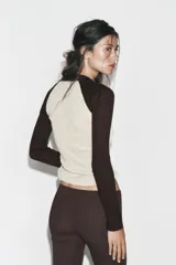 Camiseta de manga larga, corte slim fit, con cuerpo color beige claro y mangas y cuello polo en color marrón oscuro. Presenta un escote en pico bajo el cuello polo.