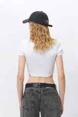 Top blanco de corte crop, escote redondo pronunciado y mangas cortas ajustadas.