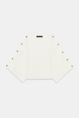 Jersey de punto blanco marfil, con cuello barco y mangas anchas tipo capa decoradas con botones a lo largo de los hombros y brazos.