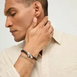 Pulsera confeccionada con múltiples tiras de cuero marrón oscuro, con piezas metálicas de diseño orgánico bañadas en plata y cierre ajustable con cadena de eslabones.