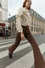 Pantalón de tiro alto color marrón oscuro, con corte flare (campana) y nervio marcado en el frente de ambas piernas. Presenta bolsillos delanteros y bolsillos de plastrón en la espalda.