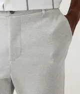 Pantalón de corte slim color gris claro, confeccionado en tejido de poliéster con mezcla de algodón y elastano. Presenta cintura elástica con trabillas, cierre frontal con botón y cremallera, y bolsillos laterales y traseros.