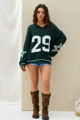 Sweater de punto color verde oscuro, con diseño oversize, mangas largas con estrellas blancas estampadas y la inscripción "BOSTON 29" en la espalda.