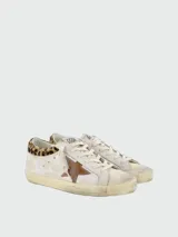 Zapatillas Golden Goose modelo Super-Star, fabricadas en cuero blanco con efecto envejecido, estrella lateral de cuero marrón, refuerzo trasero con estampado animal print tipo leopardo y suela desgastada.