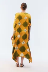 Kaftan maxi amplio de color amarillo, con escote redondo, mangas cortas y ruedo irregular. Presenta un diseño estampado a cuadros con efecto teñido.