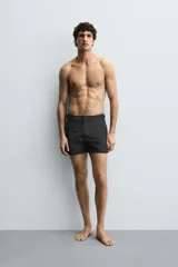 Bañador de hombre color negro, de largo medio, confeccionado en tejido técnico. Presenta cintura elástica ajustable con cordón interior, trabillas laterales, bolsillos frontales y bolsillo trasero con cierre de cremallera.