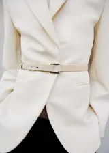 Blazer color crema con cuello de solapa, hombros marcados, bolsillos delanteros, cinturón desmontable y forro interior.