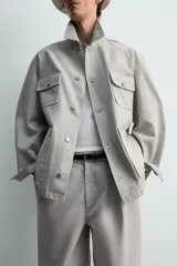 Cazadora de corte relajado confeccionada en tejido de algodón compacto con efecto lavado. Presenta cuello de solapa, manga larga con puños abotonados y cierre frontal de botones. Incluye cuatro bolsillos frontales: dos de plastrón con solapa en el pecho y dos bolsillos dobles de plastrón en la cadera.