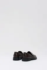 Mocasín de estilo clásico en color chocolate, confeccionado en cuero sintético liso con detalle de empeine en pelo sintético con estampado de manchas de vaca.