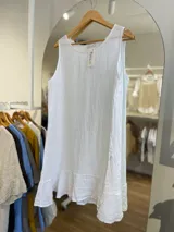 Vestido corto sin mangas, color gris topo, con escote redondo y detalle de volado en el ruedo. El tejido presenta una textura arrugada característica del lino.